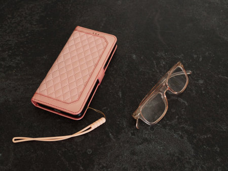 Close-up of a smartphone in a pink case and pink reading glasses on a dark background.