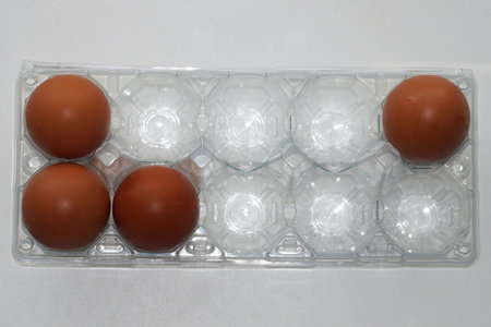 Close-up of fresh brown eggs in a transparent plastic carton on a light background for healthy diet,...