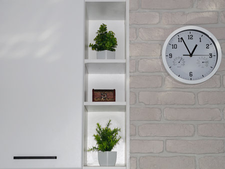 A modern interior with a wall clock and green plants on white shelves against a brick wall. A minimalist home decor concept symbolizing order, freshness, and modern design.の写真素材