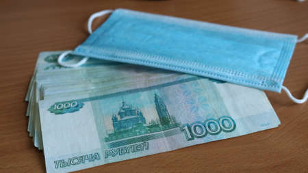 a pack of Russian bills of one thousand rubles scattered on the surface of the table and a clean blue medical mask symbolizing individual protection from the virusの写真素材