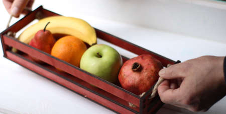 male hands hold a decorative wooden box with different fruits on a white background