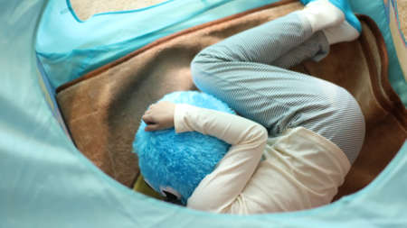 girl hugs a plush round toy and lies on a soft blanket in a blue game tent in a room top viewの写真素材