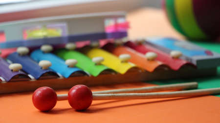 multicolored metal xylophone with wooden sticks located on a blurred background of other colored children's toys, a rubber ball and a plastic tambourineの写真素材