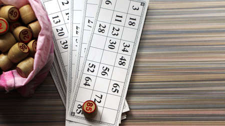white cards with black numbers and wooden numbered barrels in a pink textile bag for playing loto on a light striped background top viewの写真素材
