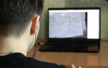 a young man from the back sits at an empty table in front of a blurred laptop monitor with...