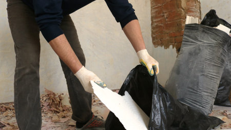 a cleaning worker in a dark uniform collects construction waste with his gloved hands in a cluttered...