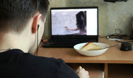 a student attending an online lecture from his home using a laptop and the Internet and a girl...