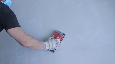 partially visible repairman in the face of a mask with a red wall sander in his right hand against...