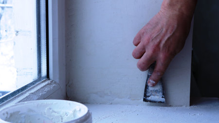 manual repair work with a narrow spatula on the plaster of a window slope, a man's hand with a...