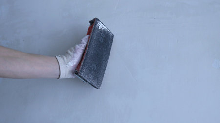 hand in a glove with emery on the background of a gray wall, an example of a construction tool in hand, a repair backdrop with a place for text, an image of a repairman with an emery meshの写真素材
