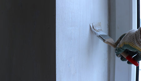 painting the surface of the slope of a plastic window with a narrow brush, applying a white water-based emulsion to the wall with a gloved hand with a brush, updating the interior of the roomの写真素材