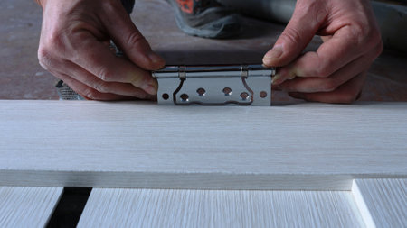 installation of door fittings made of shiny metal close-up, fixation of door hinges in the process of fitting the door leaf to the door frame, an element of the carpenter's work processの写真素材