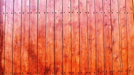 a fragment of a rustic fence made of textured wood covered with a red stain and protective varnish,...