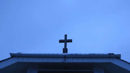 a simple Christian cross located on the roof of a building against the background of a cloudy winter...