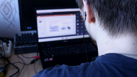 education and work at a distance from home, a guy in headphones at work and study in front of a laptop screen, classes and lectures on video communication, computer technologies in everyday lifeの写真素材