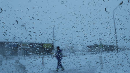 a look through glass in drops of wet snow at a pedestrian walking along the street, a blurry view of...
