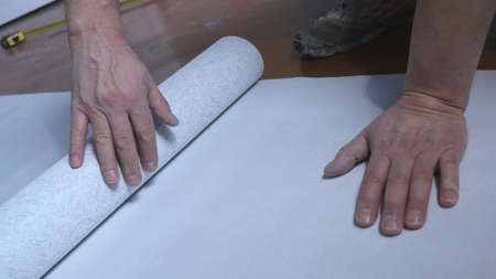 male hands roll out a roll of wallpaper on the floor of a room, close-up, a worker measures the size...