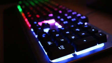 blurred view of black computer keyboard with multicolored neon backlit letters and signs with focus on the corner key Enter, messages and queries in the field of computer communicationの写真素材