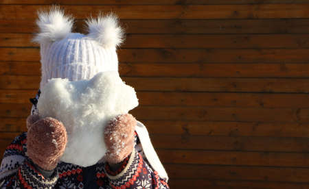a girl on a winter walk holds a heart-shaped snowball in her hand covering her face, winter fun of...