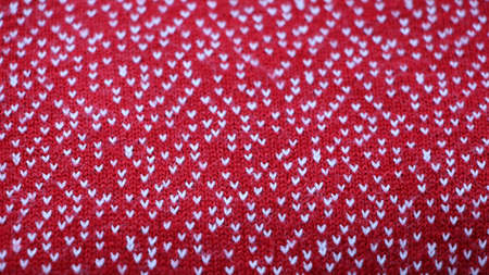 soft red woolen fabric with a pattern of white stitches as a traditional winter cozy backdrop, a fragment of a warm woolen sweater, a background associated with comfort and warmthの写真素材