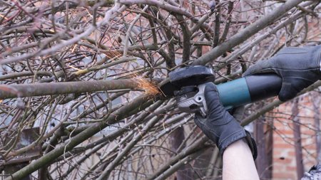 hands of a man in thick protective gloves sawing an iron rod in a vine garden with sparks flying...