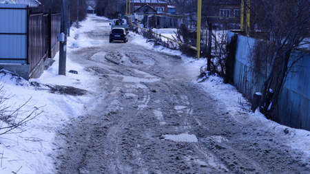 Maykop, Adygea republic, Russia - March 13, 2021: poor spring road in pits and puddles from melting snow in a Russian village, no roads in Russiaのeditorial素材