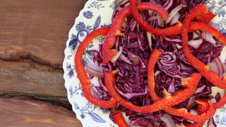 food background of fresh bright vitamin vegetables, red cabbage and red bell pepper vegetable salad on white plate with blue pattern top view, veggie snack from cut organic vegetablesの写真素材