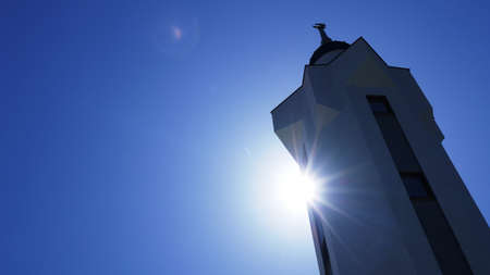 white tower from the ensemble of a mosque with a muslim symbol of a crescent moon on a background of blue clear sky and sun rays, islamic faith religious conceptual backgroundの写真素材