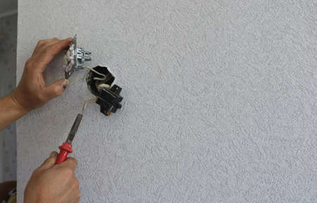 hands working with replacement of a switch against the background of an empty room wall, background...