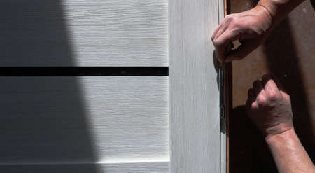 installation of metal hinges on a light door leaf by the hands of an assembler, the background of...