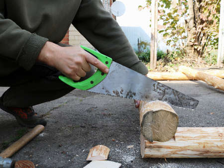sawing off a part of a log during the construction of a wooden blockhouse in a village, working with a hacksaw with wooden material, village woodworkの写真素材