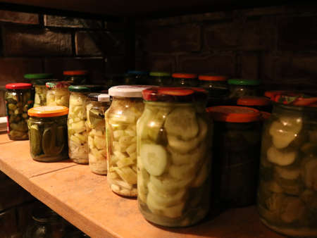 jars of canned homemade cucumbers on the shelves of the cellar, pickled vegetables in glass jars in the interior of the basement, stocks of pickled cucumbers in canned formの写真素材