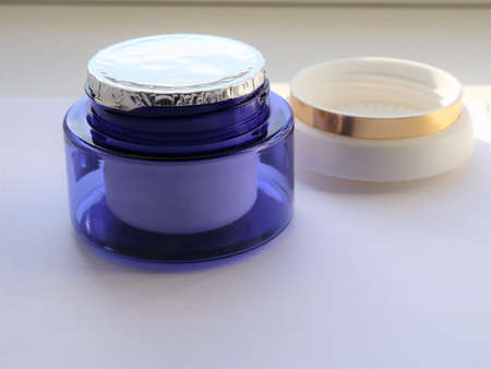 a blue plastic jar of cream with a sealed foil on top and a light lid with a gold border behind on a light background, an unused object of women's face skin care cosmeticsの写真素材