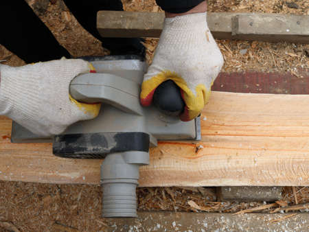 electric planer in the hands of a carpenter processes the surface of a log top view, smoothing a...