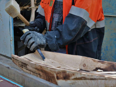 craftsman working on wood with a chisel and a mallet in a street workshop, making a tray for washing...