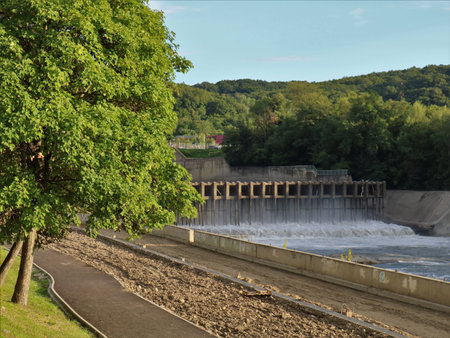 an old dam with a road bridge at the top, standing on the river, visible from the side of the embankment in the city park, a small pressure of water flowing through the locksの写真素材