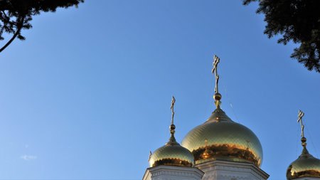 three gilded domes with Orthodox crosses against a clear blue sky framed by tree branches as a religious background with copy space, abstract banner on the theme of Orthodoxyの写真素材