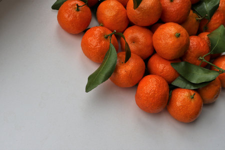 <p>ripe orange tangerines with green leaves occupying the upper right side of the space and a light copy space in the lower left corner, a display of citrus fruits on a white surface</p>の写真素材
