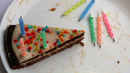 the last lonely piece of birthday chocolate cake with several extinguished colorful candles on a...