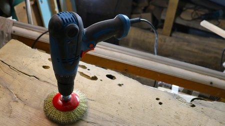 blue electric drill standing on a round mounted brush with metal bristles on a wooden surface in a...