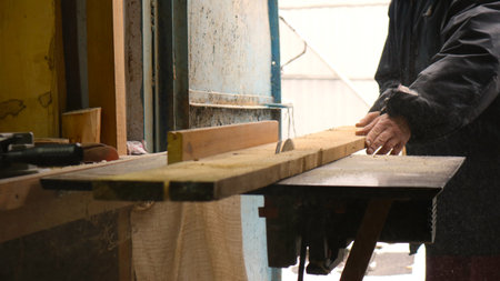 carpenter's workshop with a homemade circular saw and sawing a rough long board lengthwise, a...
