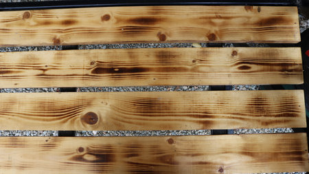 textured background of separate stained wooden planks with natural pattern on gray gravel background, fragment of bench made of wood with processed boards in structureの写真素材