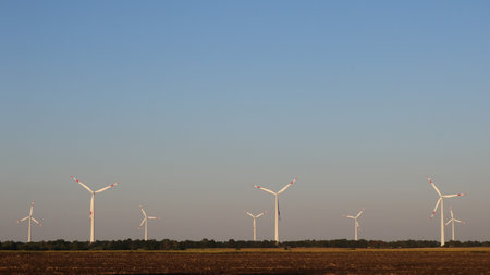 agricultural field with several wind turbines in the distance against a clear sky, wind and solar...