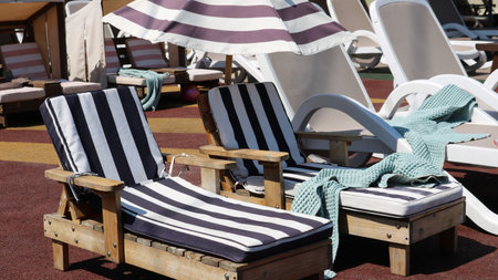 two children's wooden sun loungers with soft cotton striped cover next to adult lounge chairs under...