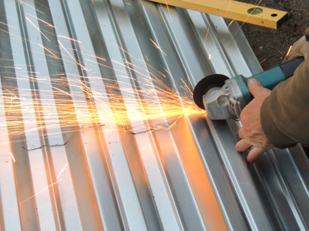 hands with grinder sawing corrugated gray shiny sheet of iron with bright sparks, grinding metal...