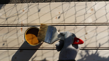 hand in glove holding brush over paint or varnish can over textured light boards top viewの写真素材