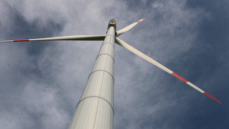 bottom view of tall wind turbine with spinning blades against stormy dynamic sky, wind generator...