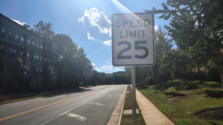 A 25 mph speed limit sign on a road between a park and an apartment building in the United States on...