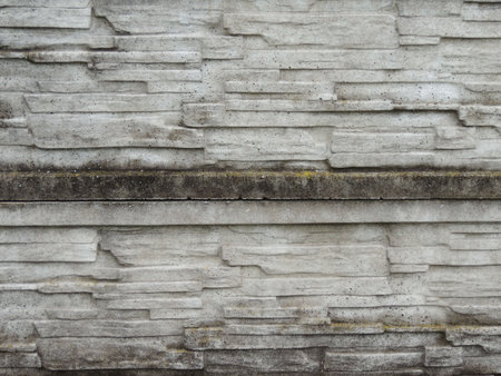 a fragment of an old, dilapidated, mossy concrete-stone fence with a rough, destroyed texture of the...