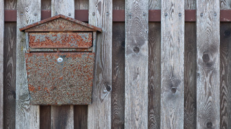 Old metal mailbox with a touch of rust hanging on the textured planks of a rustic fence, retro...
